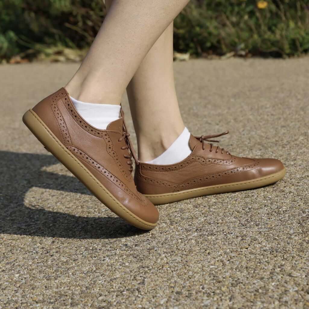 model standing outdoors wearing maple brogue barefoot shoes in tan