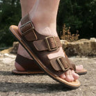model standing outdoors wearing mens acacia back strap barefoot sandals in brown