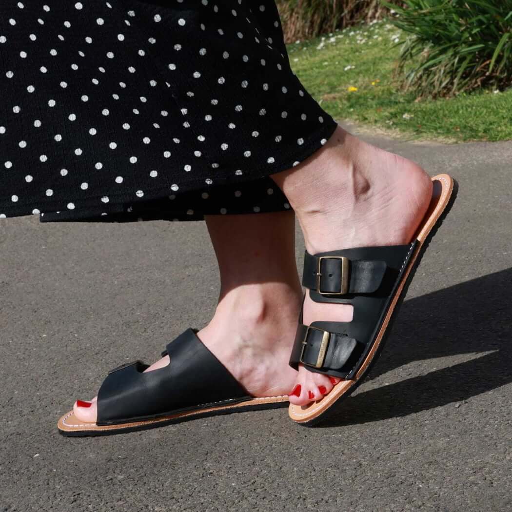 model wearing black acacia womens leather barefoot sandals with black spotty trousers on a pavement