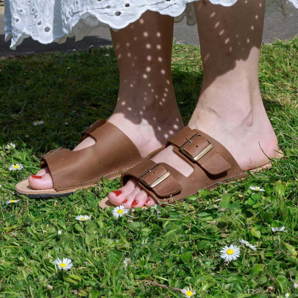 model wearing acacia womens leather barefoot sandals in tan standing on grass