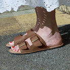 model standing outdoors with acacia womens leather barefoot sandals in tan being worn with a white dress