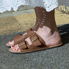 model standing outdoors with acacia barefoot sandals in tan being worn with a white dress
