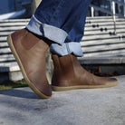 model wearing brown chelsea boots in sunny setting on concrete with jeans