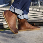 model wearing brown chelsea boots in sunny setting on concrete with jeans