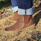 model wearing brown leather barefoot boots with jeans on gravel path outdoors