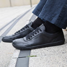 model sitting on steps wearing aspen black barefoot trainers with dark jeans