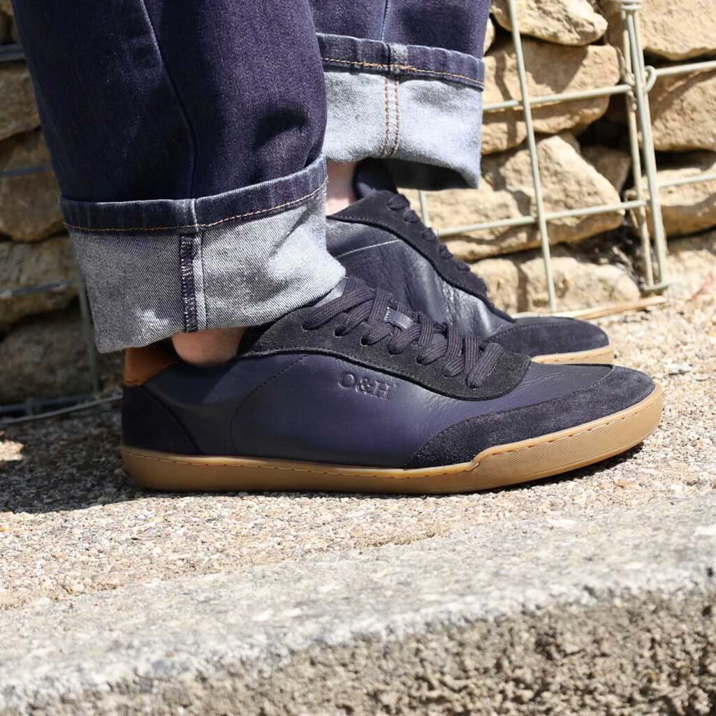person wearing dark blue aspen barefoot trainers on concrete pavement with blue jeans