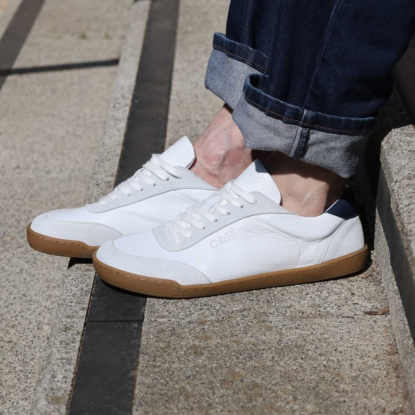 model sitting on concrete steps showing side view of white aspen barefoot trainers