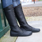 side view of person wearing tall black barefoot boots with jeans on pavement