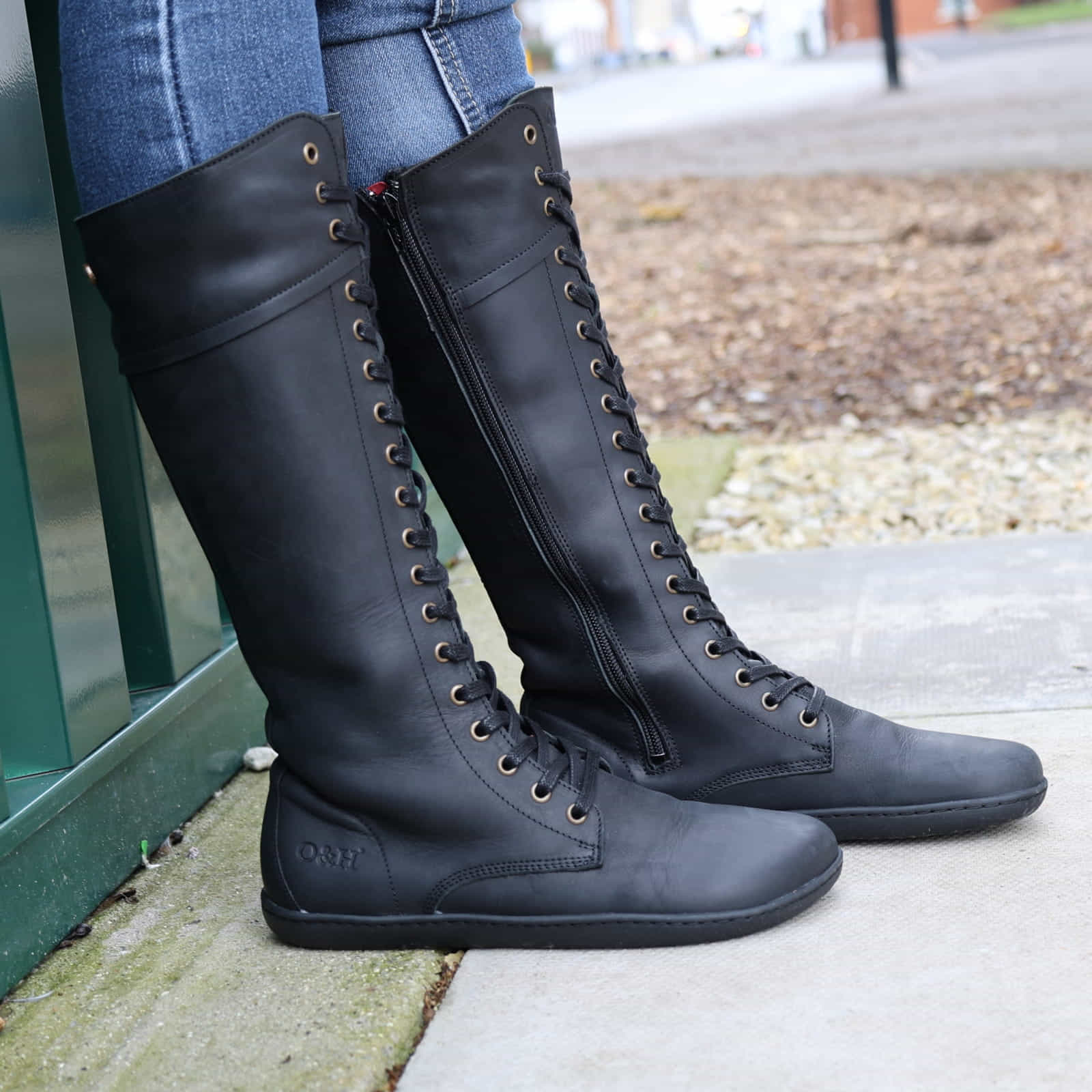 side view of person wearing tall black barefoot boots with jeans on pavement