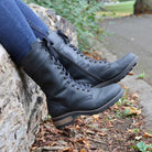 model wearing bridge 12 boots in black sat on a log worn with blue jeans