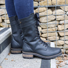 Black Bridge 12 military boots worn with jeans standing beside a stone wall outdoors