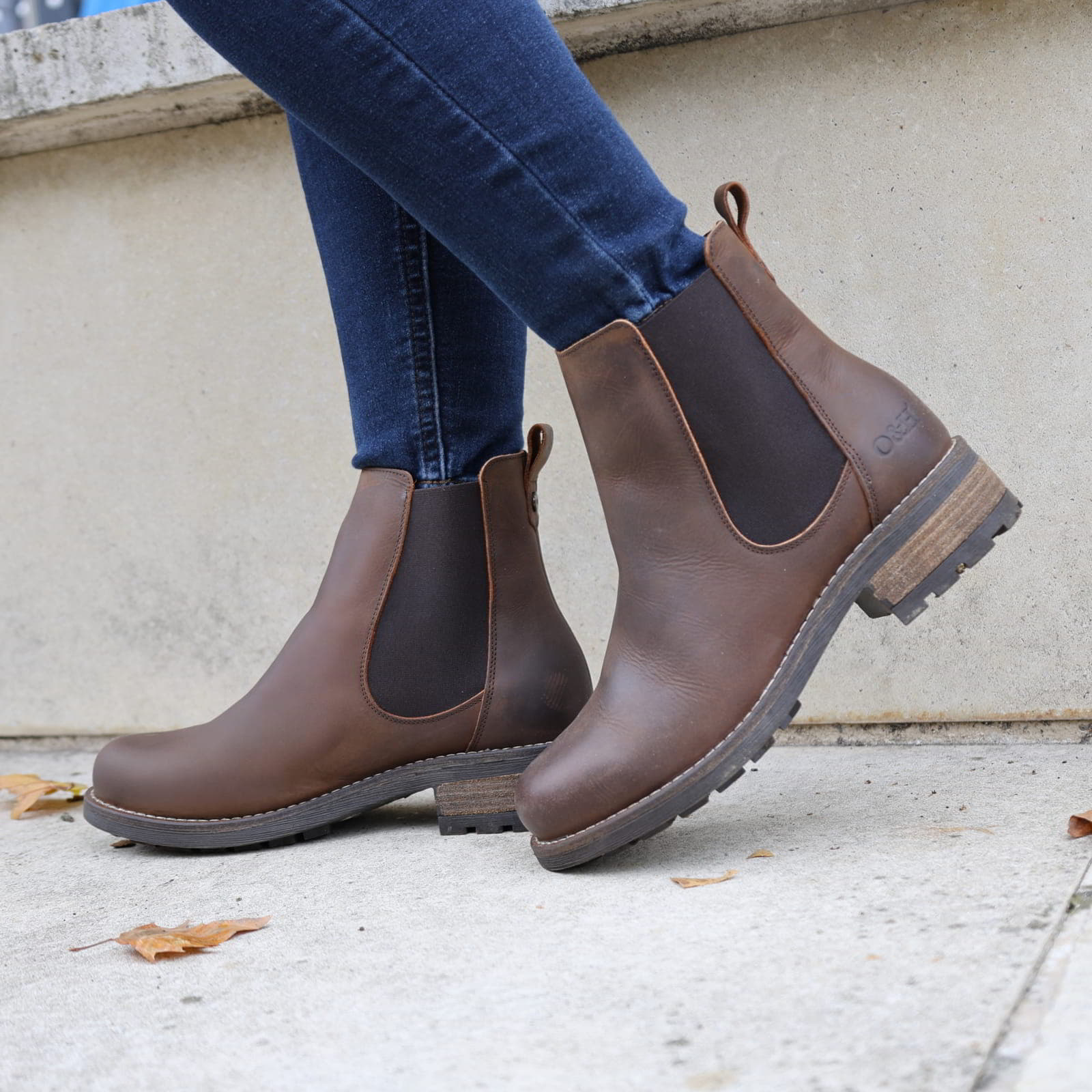 Dark brown Bridge Chelsea 2 boots worn with jeans walking beside a stone wall