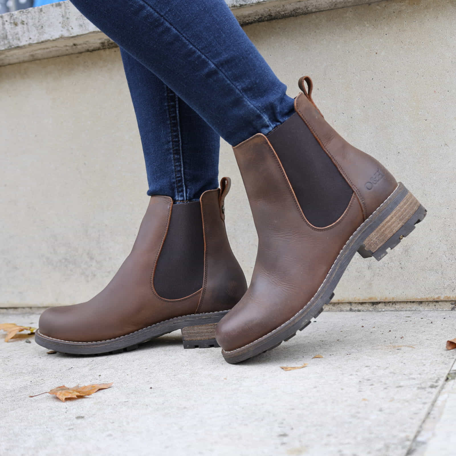 Dark brown Bridge Chelsea 2 boots worn with jeans walking beside a stone wall