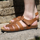 Tan leather fisherman sandal with adjustable strap and cork footbed, worn outdoors on stone steps