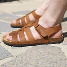 Tan leather fisherman sandals worn on foot while standing on sunlit stone paving outdoors