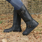 model standing outdoors wearing the cedar barefoot boots in black with blue jeans