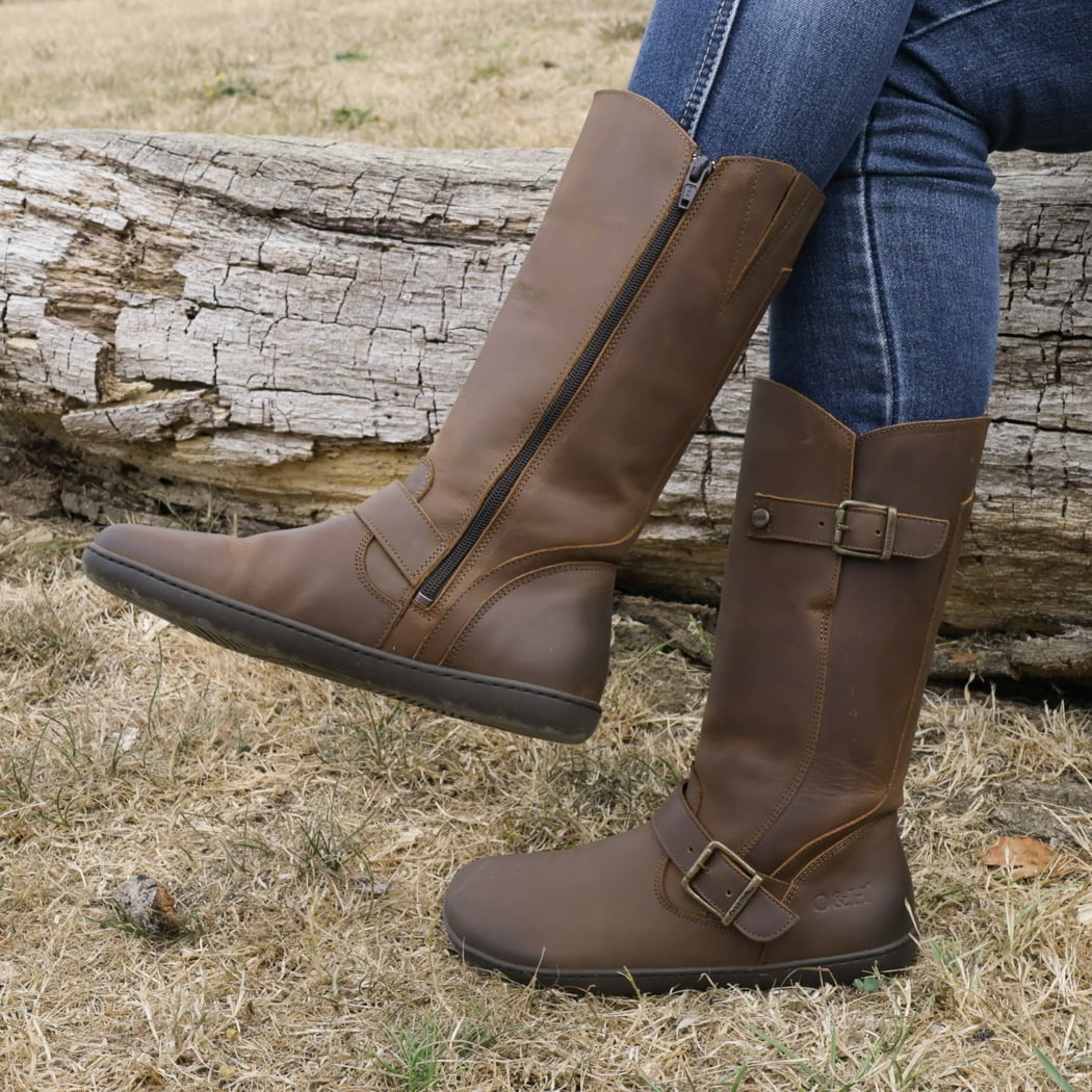 model sitting outdoors on tree trunk wearing cedar barefoot boots in dark brown