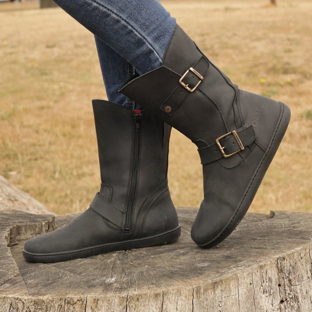 model standing outdoors on tree stump wearing cedar demi barefoot boots in black