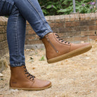 model sitting on wall wearing cherry barefoot ankle boots in cognac with crossed legs