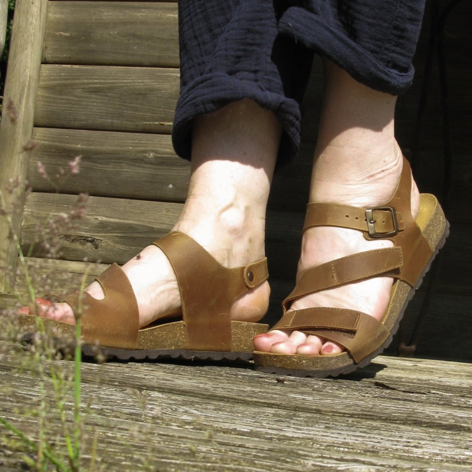 tan oak & hyde daisy sandals worn outdoors on wooden steps with rolled trousers