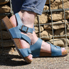 turquoise oak & hyde daisy sandals worn outdoors with rolled jeans on stone ground