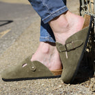 model wearing green leather clogs with jeans leaning against a stone wall