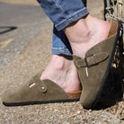 model wearing green leather clogs with jeans leaning against a stone wall