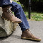 model sitting on a rock wearing mens hawthorn barefoot boots in brown