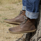 model sitting on tree stump wearing hawthorn mens barefoot boots in brown