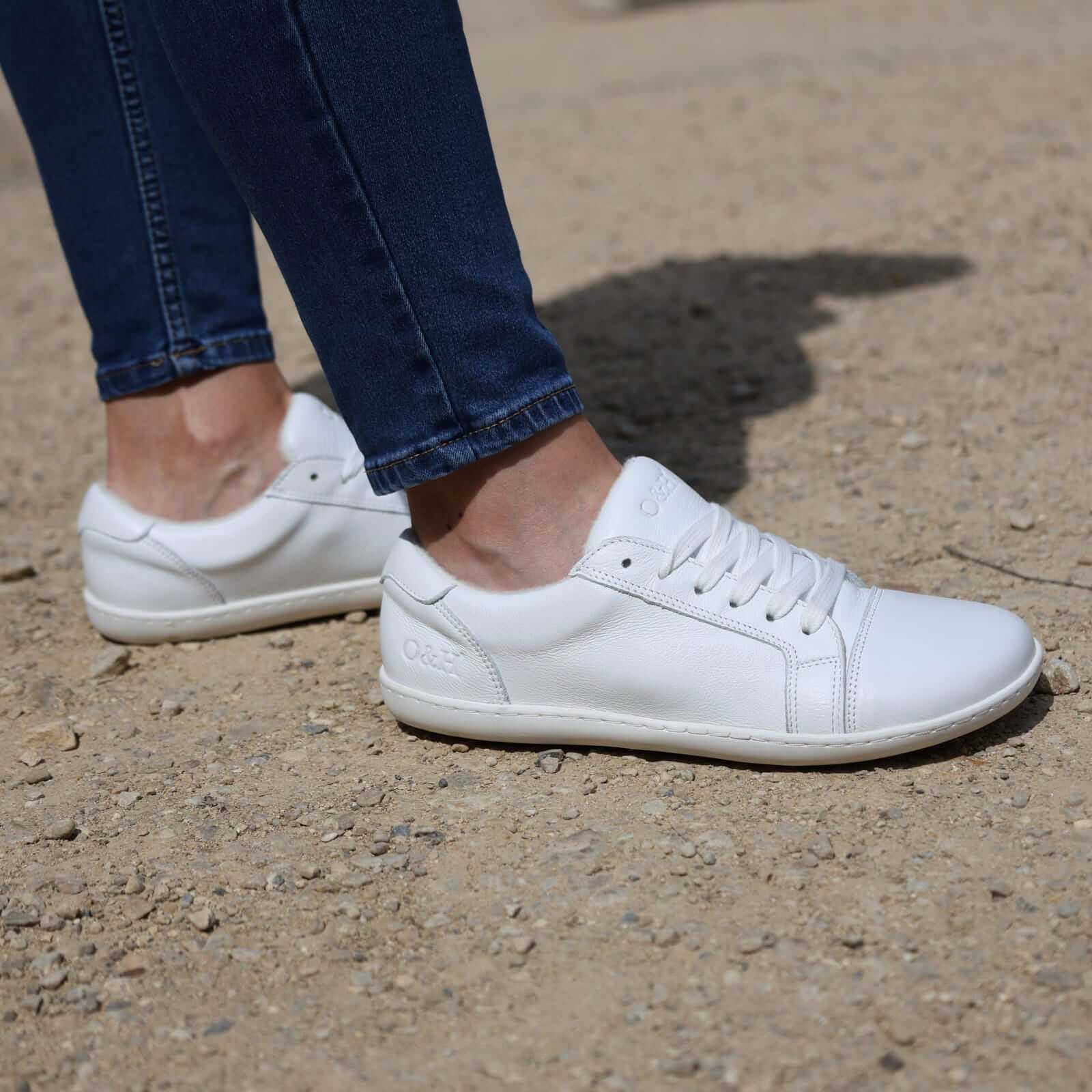 white barefoot trainers on model wearing blue jeans on pebbled ground