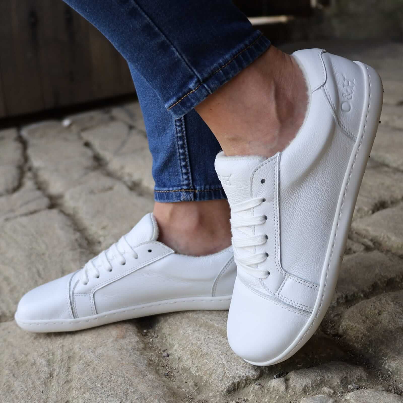 model wearing white trainers with blue jeans standing on stone pavement