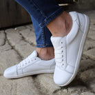 model wearing white trainers with blue jeans standing on stone pavement