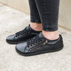 Model wearing hazel zip trainers in black standing on concrete path