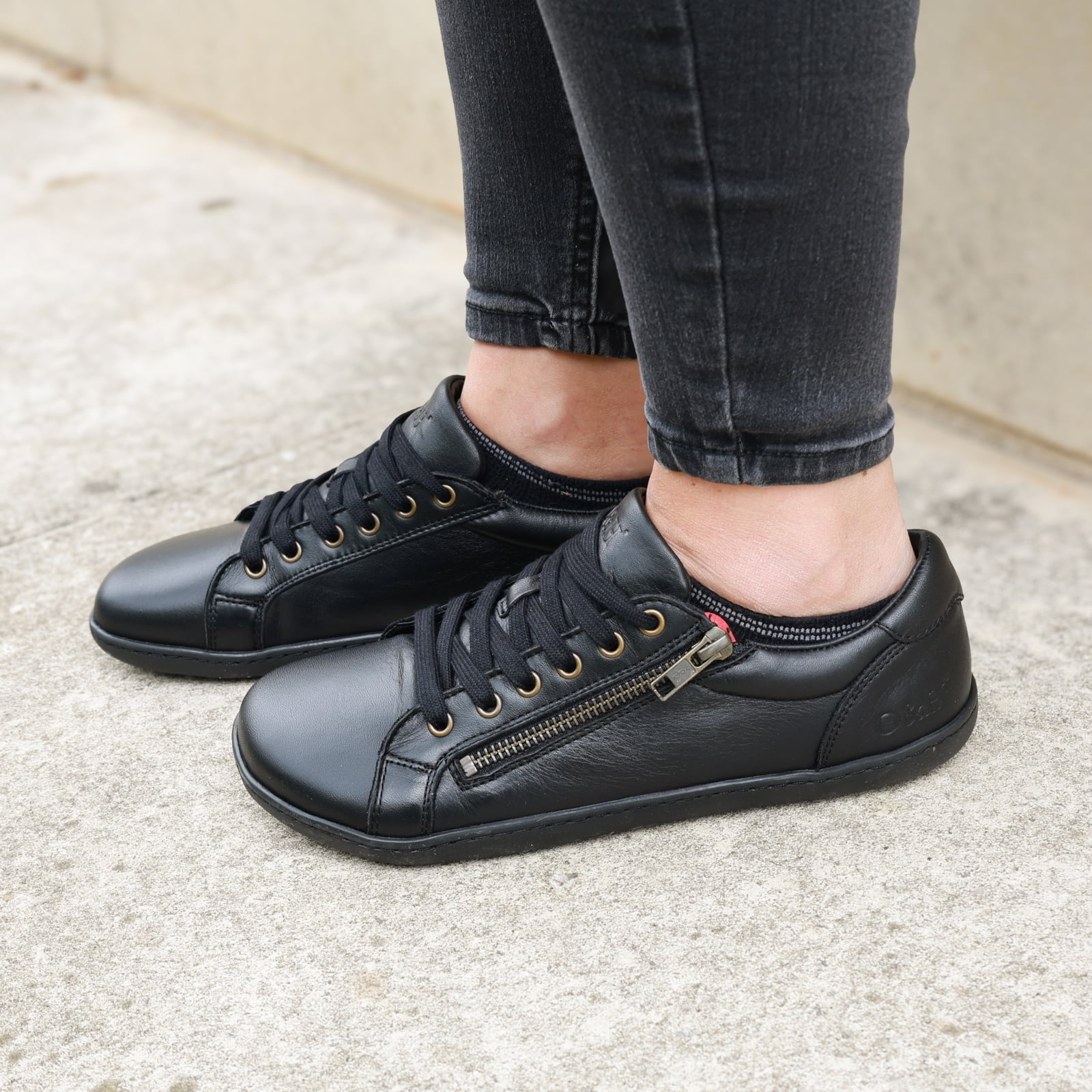 Model wearing hazel zip trainers in black standing on concrete path