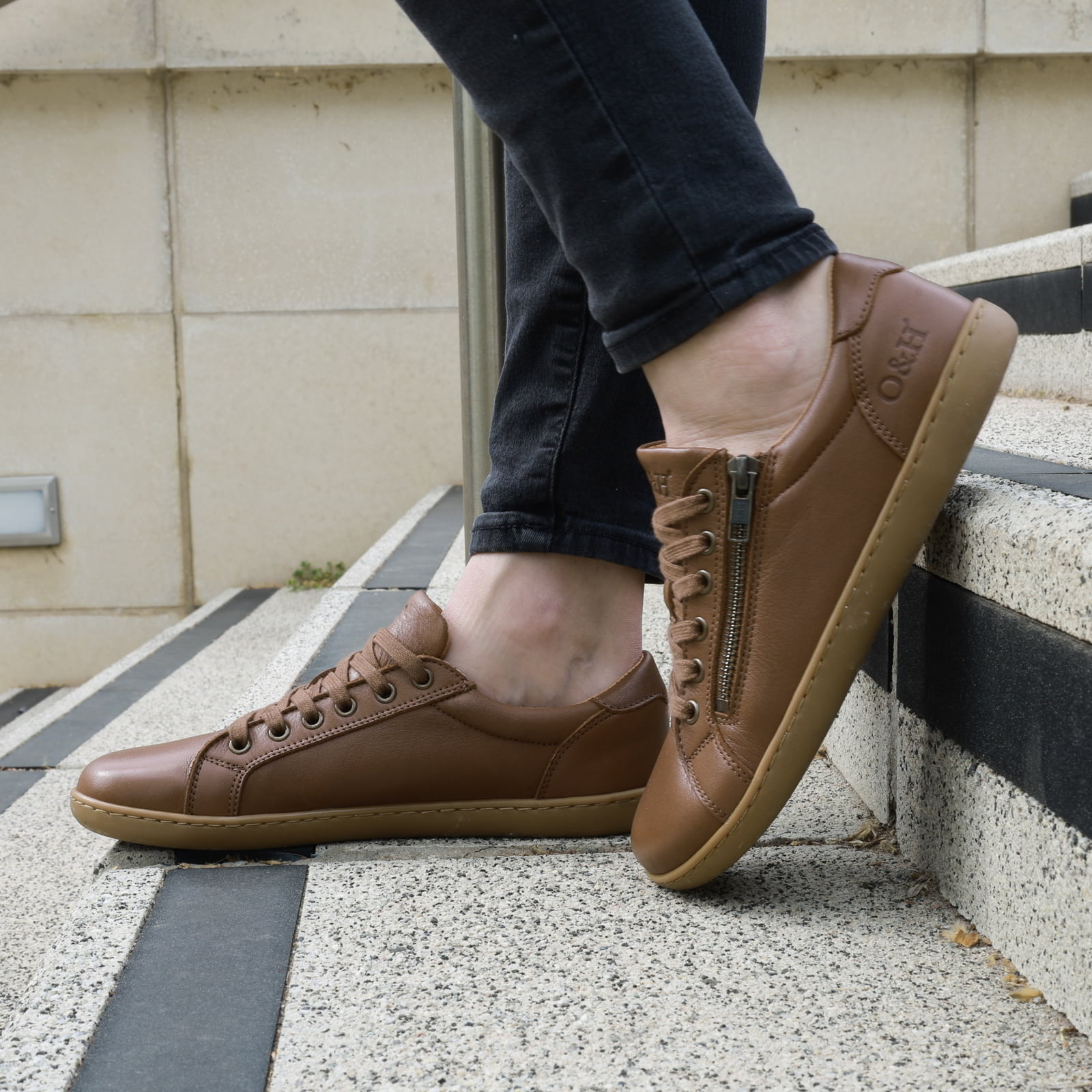 model on steps in the hazel zip barefoot shoes in tan wearing them with dark jeans