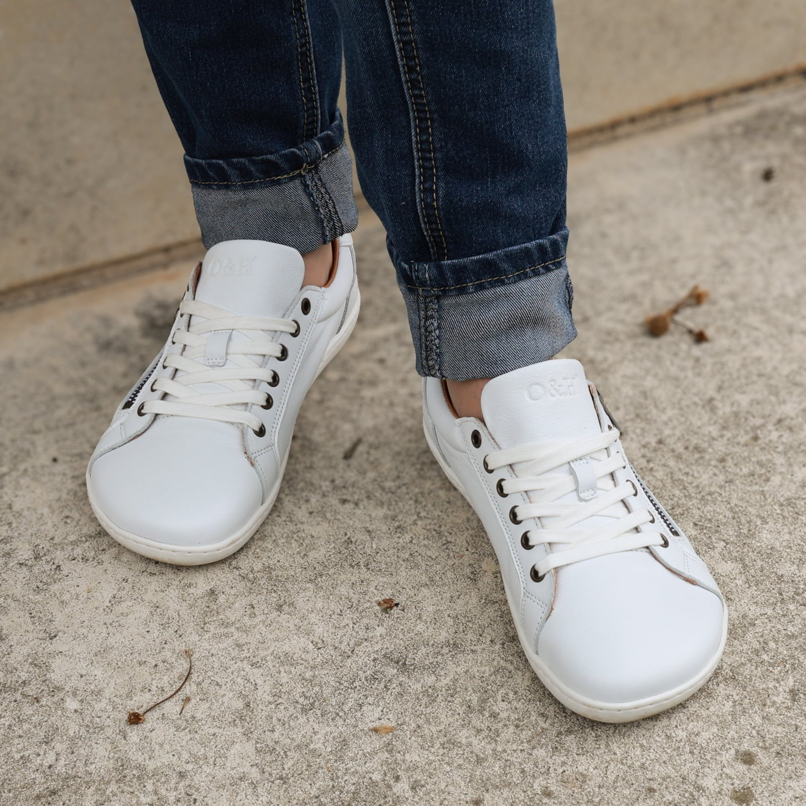 model standing outdoors in hazel zip barefoot trainers in white showing front laces