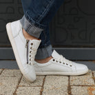 model standing outdoors wearing hazel zip barefoot trainers in white with blue jeans