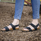 black oak & hyde iris adjustable sandals worn outdoors on bark ground with jeans