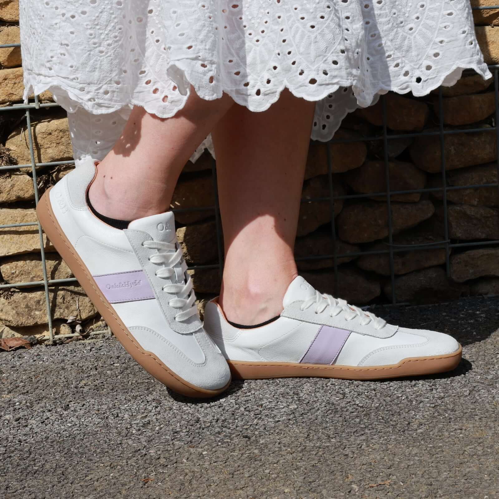 person wearing white lilac juniper barefoot trainers with a white dress stanfing outdoors