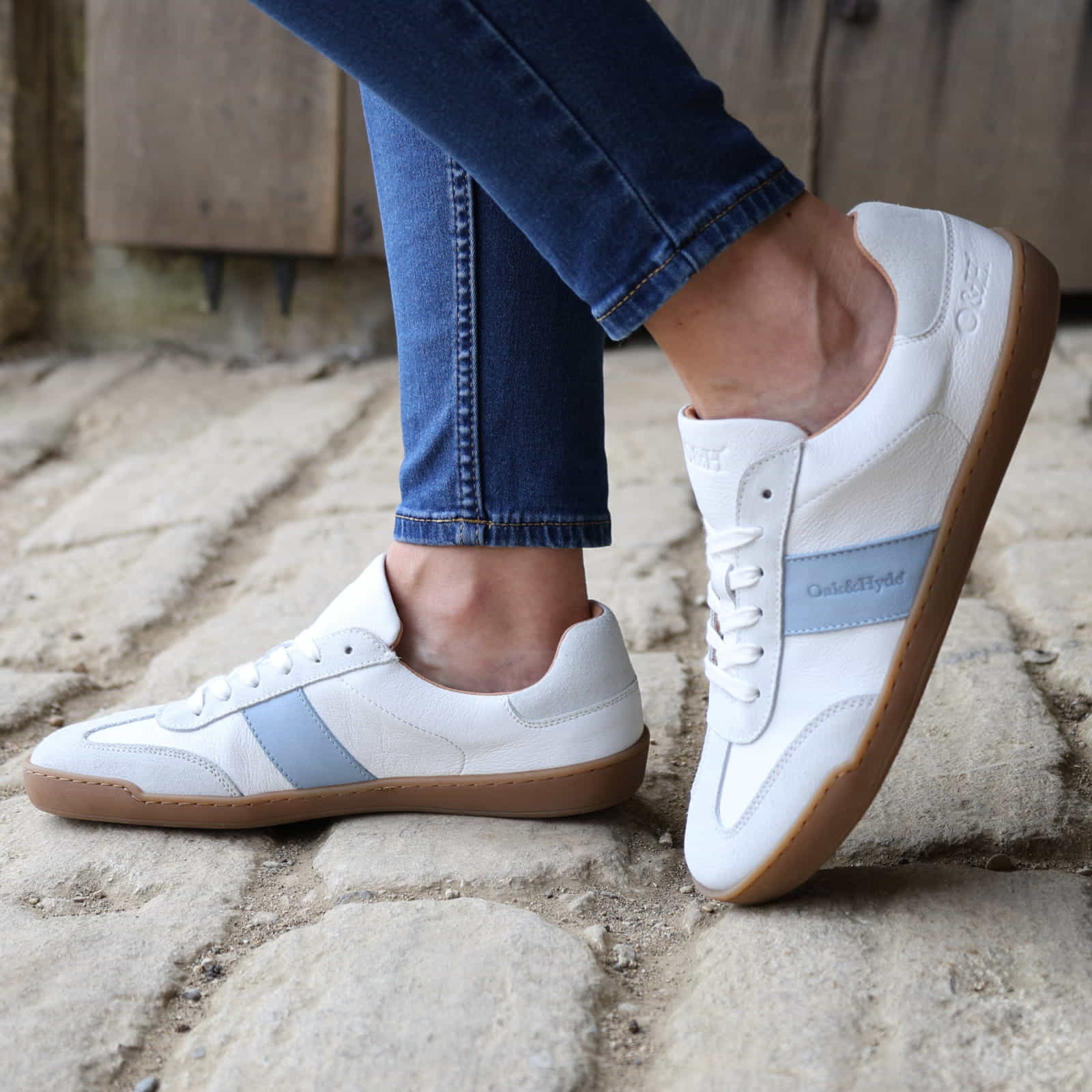 model wearing white barefoot trainers with blue jeans on a stone pavement