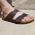 Dark brown leather fisherman sandals worn on foot on textured concrete in natural daylight