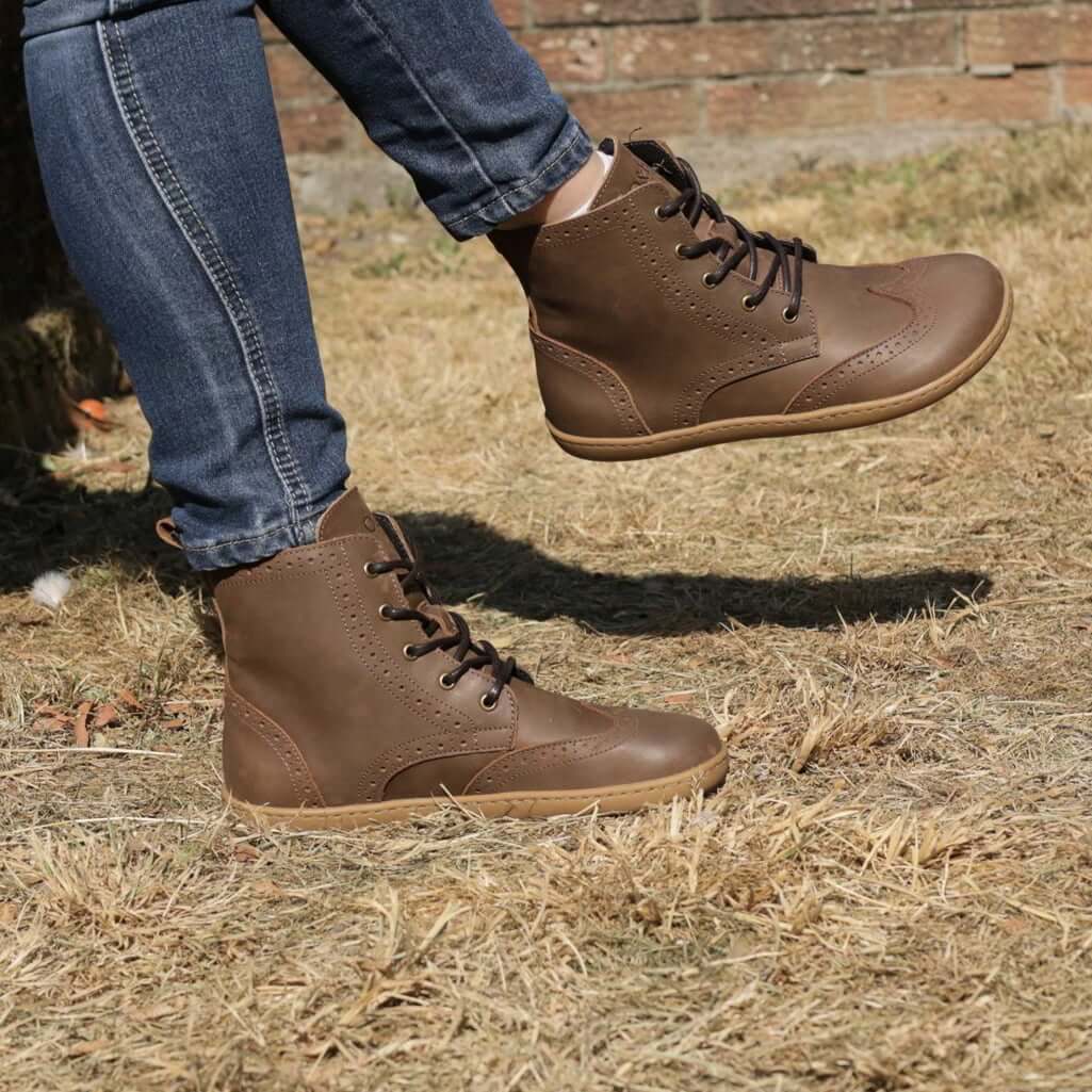 model sitting outdoors wearing maple mid brogue barefoot boots with blue jeans