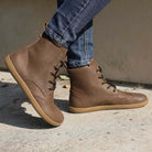 model wearing maple mid barefoot brogue boots in brown with blue jeans outdoors