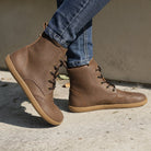 model wearing maple mid barefoot brogue boots in brown with blue jeans outdoors