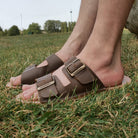 model sat in park wearing mens acacia barefoot sandals in brown showing buckles and upper