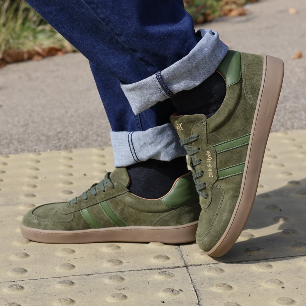 model standing outdoors in mens larch barefoot trainer in green worn with blue jeans