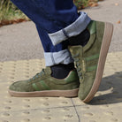 model standing outdoors in mens larch barefoot trainer in green worn with blue jeans