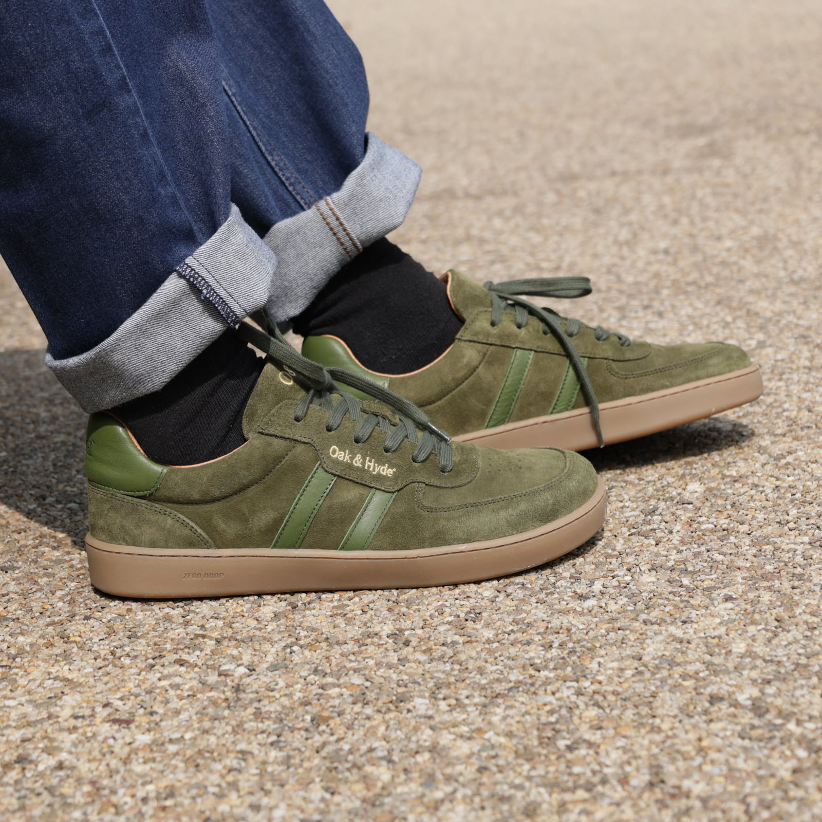 person wearing mens larch barefoot trainers in green with rolled up blue jeans