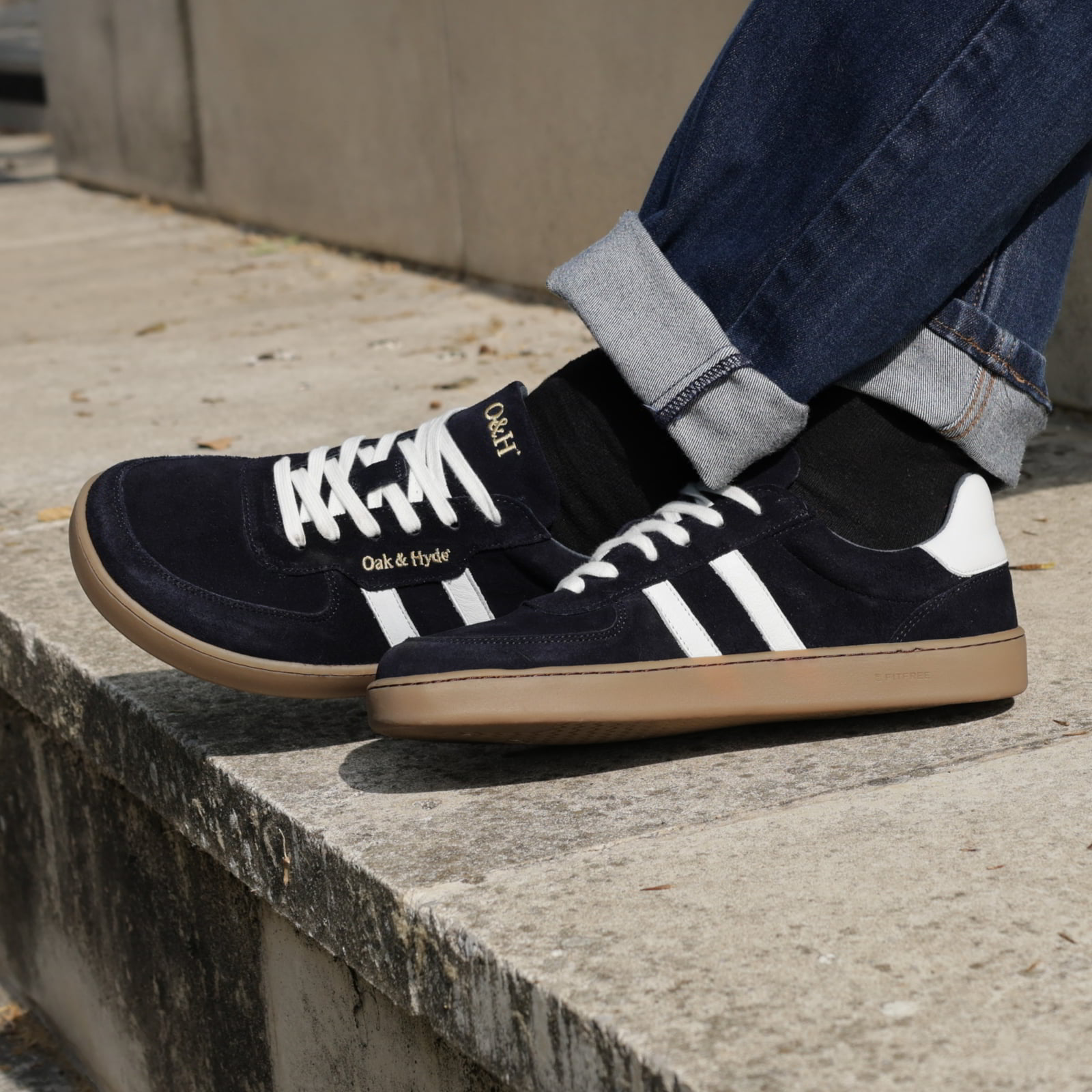 model sat on stone step wearing mens larch barefoot trainers in navy with blue jeans